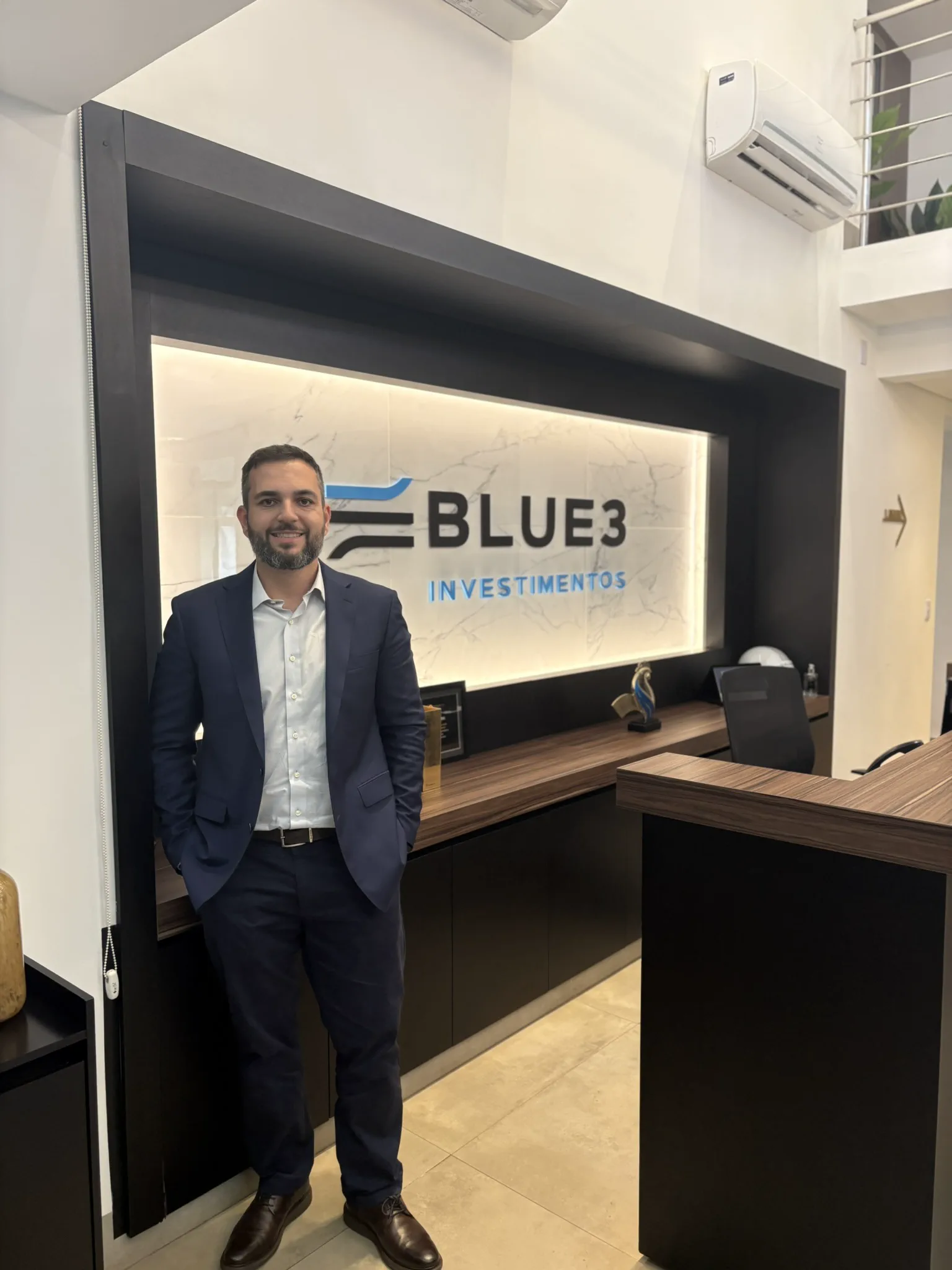 Vitor Moreira na recepção da Blue3 Investimentos, ao lado do logotipo iluminado da empresa